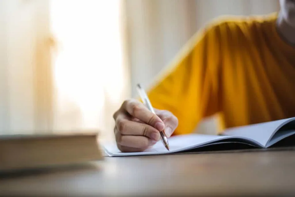 Hand holding a pen, writing on a piece of paper