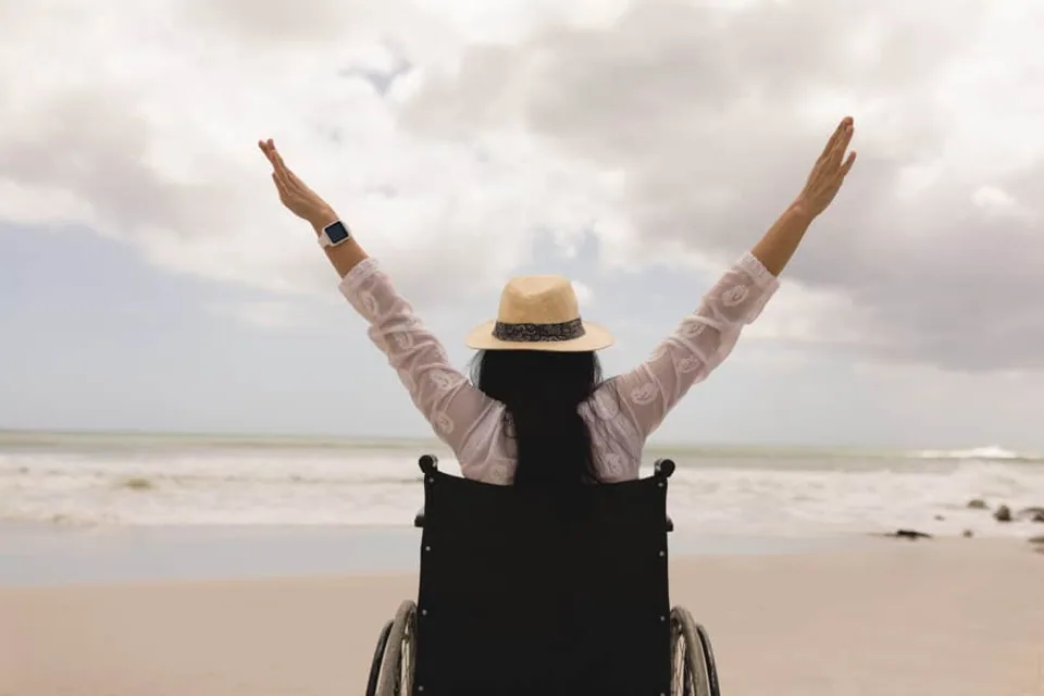 Happy lady sitting on a wheelchair lifting both hands up