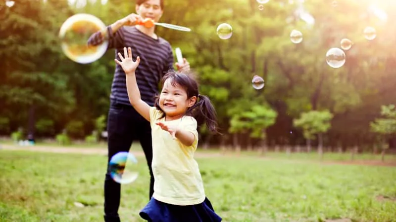 Happy little girl playing with bubbles with her dad